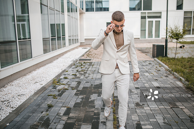 全身照：英俊的年轻男人身穿白色西装，摘下太阳镜图片素材