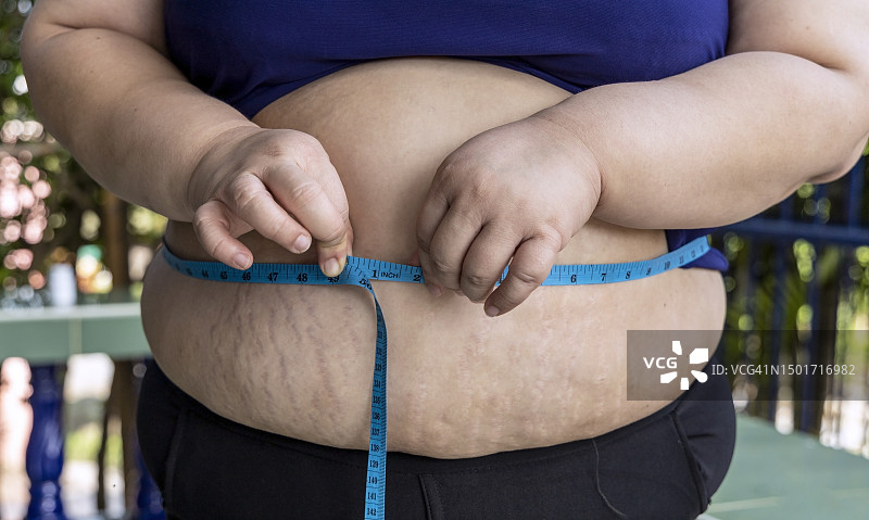减肥概念：测量腰围的肥胖女人特写图片素材