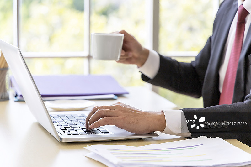 商务人士在办公室喝咖啡和使用电脑的聚焦照片图片素材