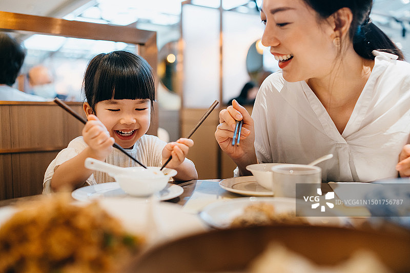 年轻的亚洲母亲和女儿在餐厅愉快用餐，享用中国美食。亚洲家庭外出用餐图片素材