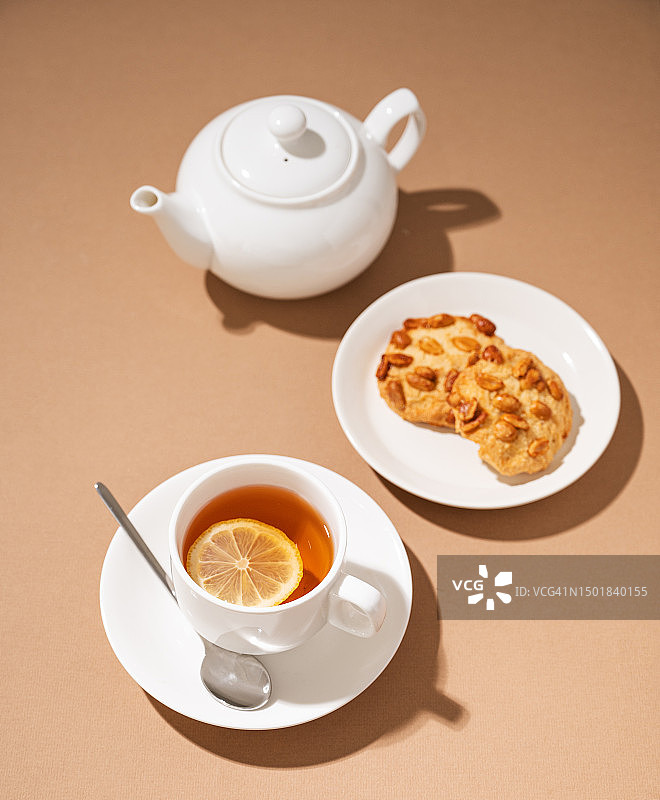一杯柠檬茶，配自制饼干和白色茶壶，健康饮品概念图片素材