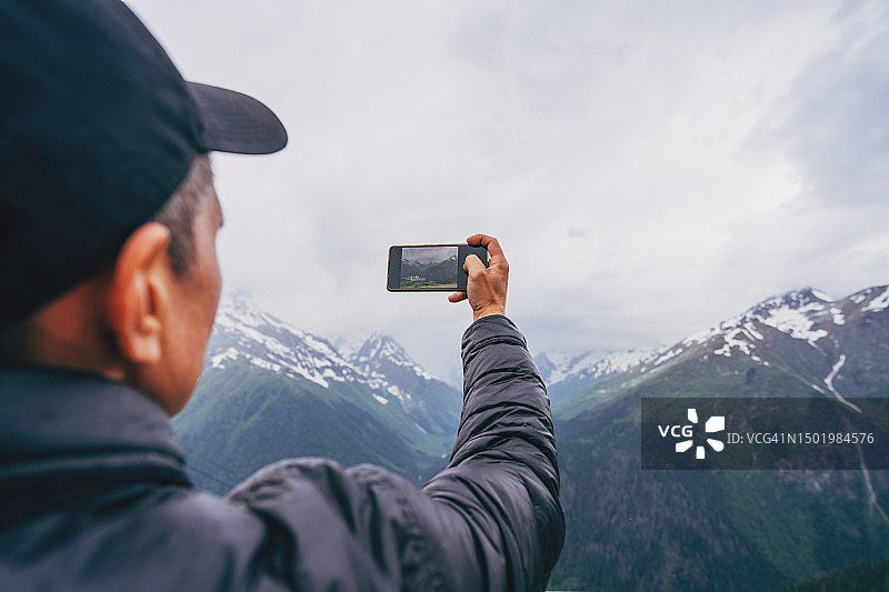 男人在阴天用手机拍摄山景图片素材