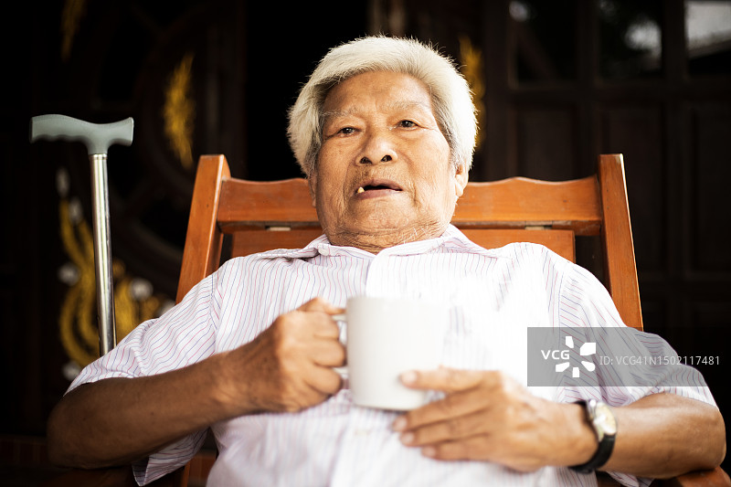 亚裔退休老人在现代住宅椅子上喝咖啡图片素材
