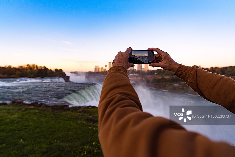 男子用智能手机在尼亚加拉瀑布拍照图片素材