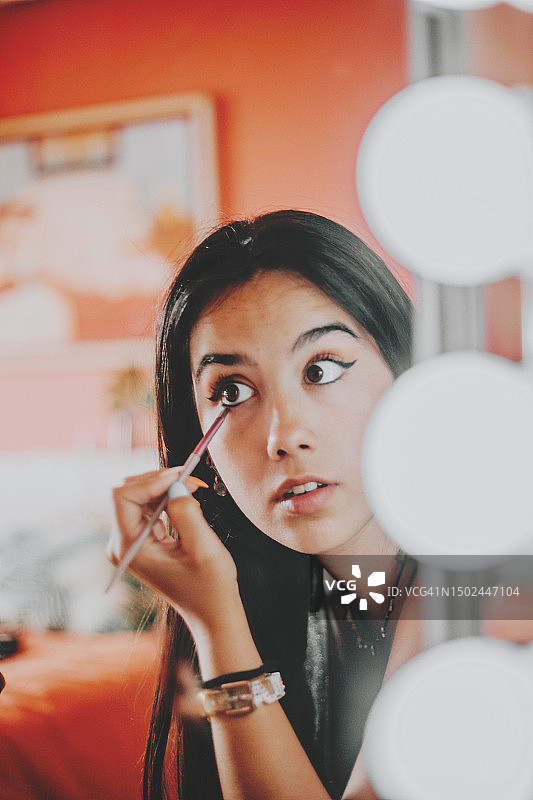 在浴室里靠近发光镜子画眼线的女人图片素材