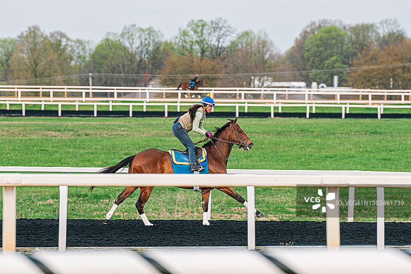 在阴天黑色人造跑道上骑马的赛马骑师图片素材