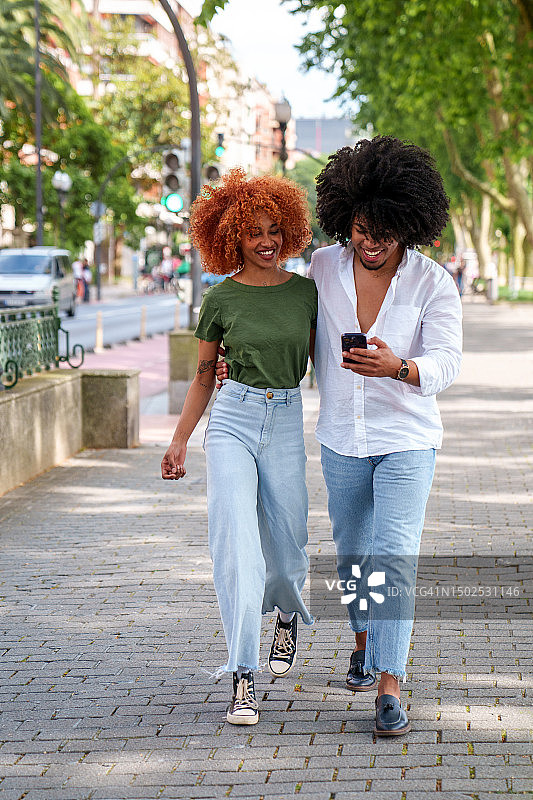 充满活力的拉丁裔朋友在城市公园分享手机乐趣图片素材