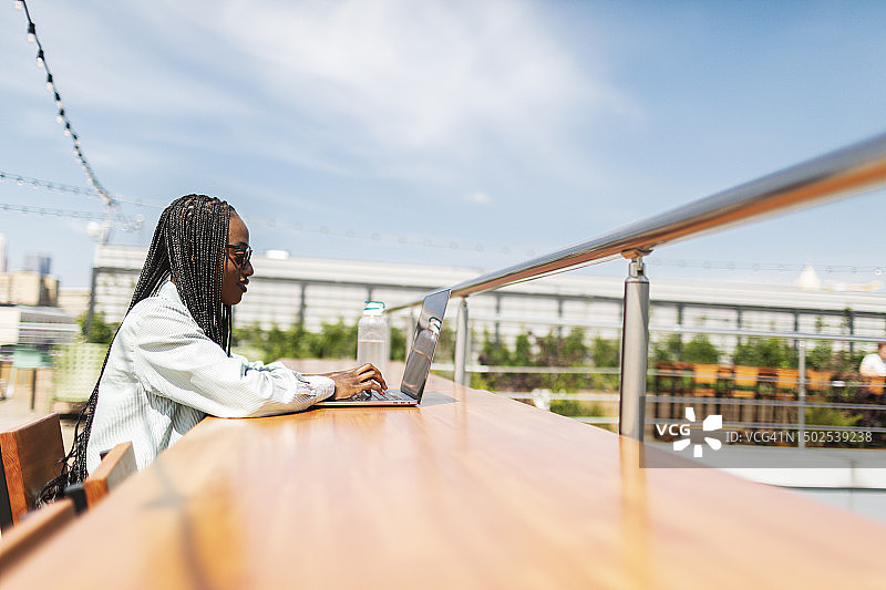 在阳光明媚的夏日，在公园户外使用笔记本电脑工作的年轻黑人女子图片素材