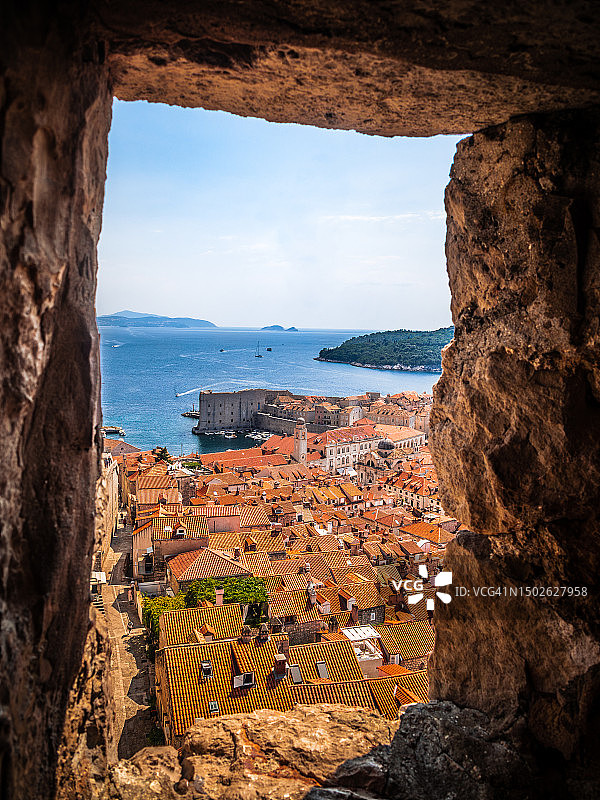 从明阙塔要塞顶部的古城墙上，透过射箭孔看到的杜布罗夫尼克老城屋顶和古老港口，达尔马提亚，克罗地亚图片素材