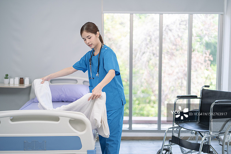 亚洲老年护理人员在医院为老人整理床铺并做家务图片素材