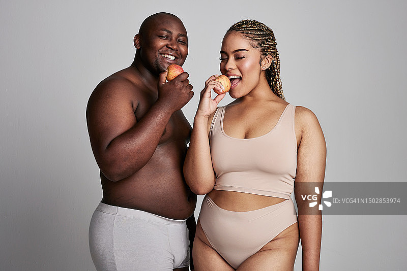 快乐情侣内衣照：非洲男女在白色背景的影棚吃苹果，健康营养饮食图片素材