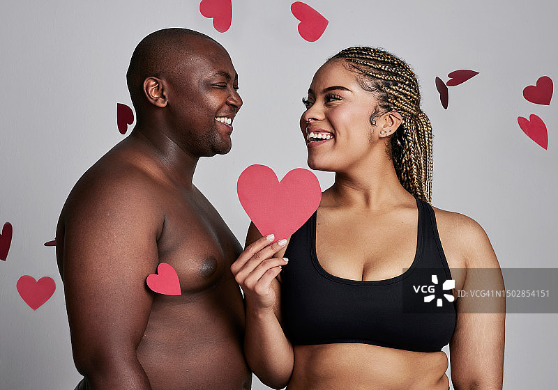 爱心，爱和加大码情侣穿着内衣，表达身体的积极性、浪漫或情人节。黑人男子和自然女性穿着内衣，带着微笑，在工作室背景上拿着红色纸和图标或形状图片素材