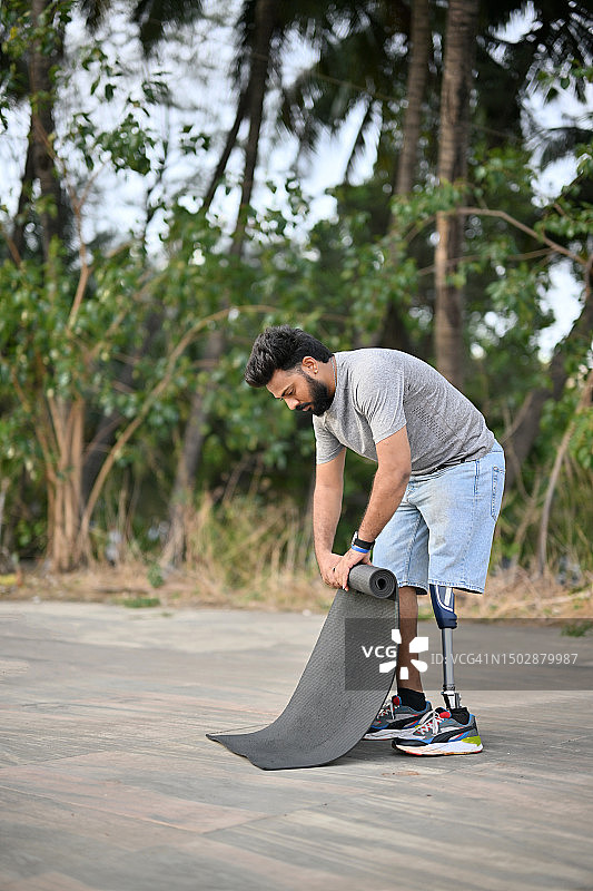 在宁静的户外瑜伽练习后，折叠瑜伽垫的假肢男人图片素材