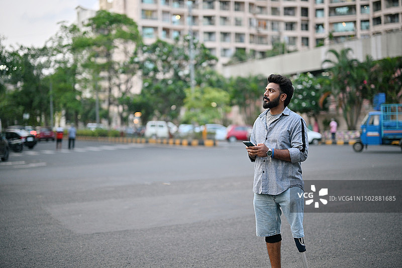 男人使用假肢和手机在城市街道上行走的肖像图片素材