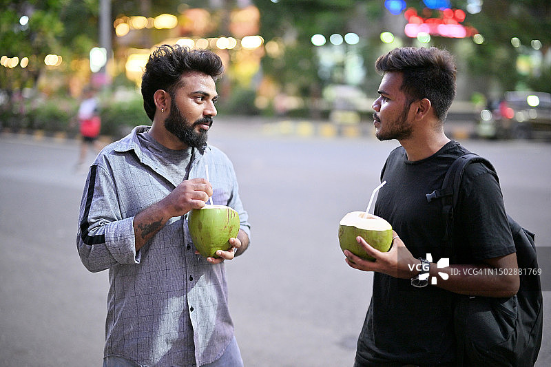 两个年轻男子在黄昏时分站在城市街道上喝椰子汁图片素材
