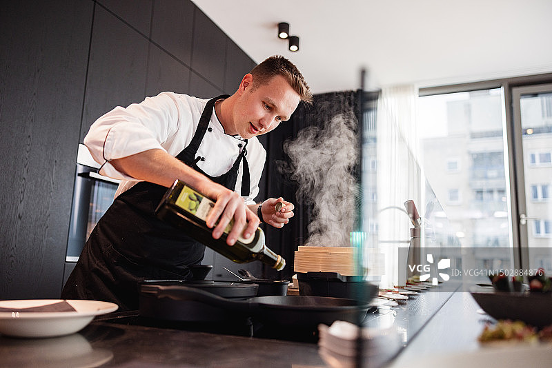穿着制服和黑色围裙在高级公寓里做饭的年轻白人私人厨师图片素材