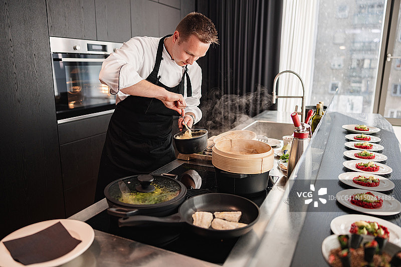 穿着制服和黑色围裙在高级公寓里做饭的年轻白人私人厨师图片素材