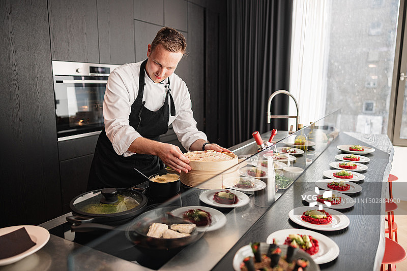 穿着制服和黑色围裙在高级公寓里做饭的年轻白人私人厨师图片素材