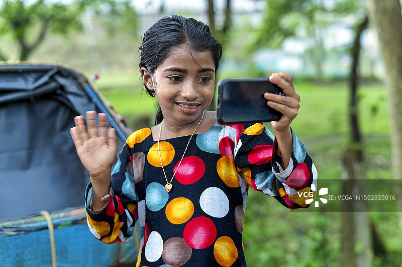 美丽的亚洲女孩在使用智能手机进行视频通话时挥手致意图片素材