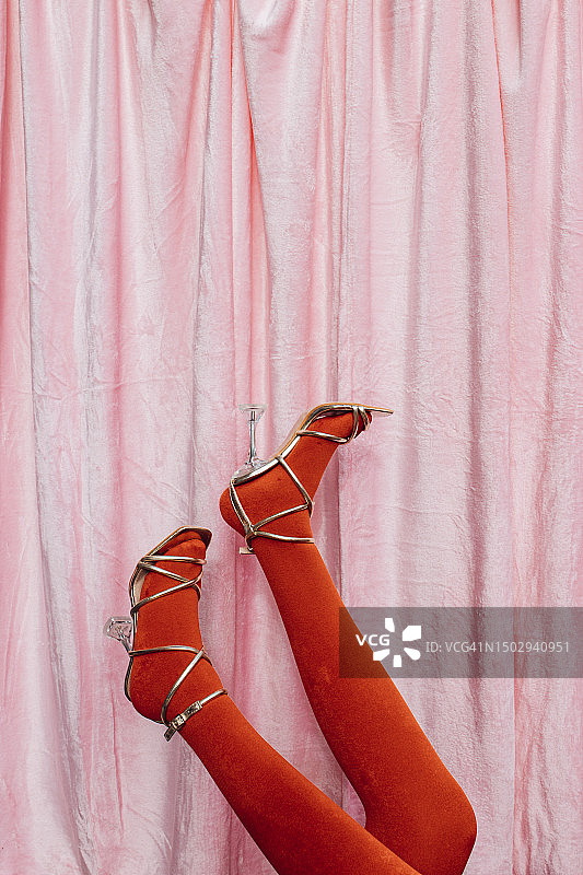一个无法辨认的女人站起来，穿着粉红色天鹅绒背景的金色凉鞋图片素材