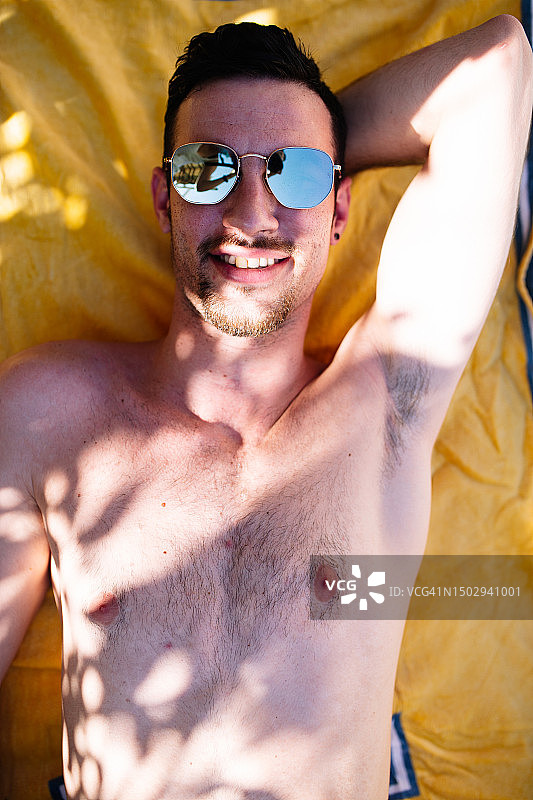 千禧一代男性躺在沙滩巾上的俯视图图片素材