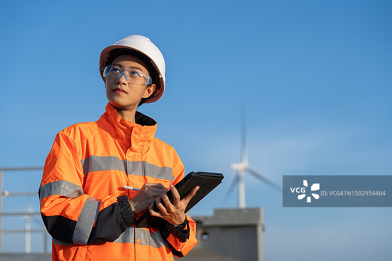 在风力涡轮机农场使用平板电脑的亚洲女性图片素材