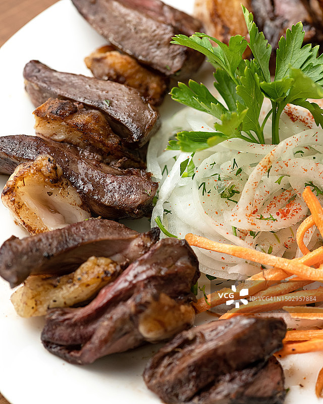 白盘子上放着胡萝卜洋葱猪肝串。用欧芹装饰的培根蔬菜炒猪肝。中东美食。木制背景。顶部视图。复制空间图片素材