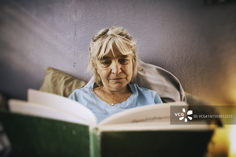 在窗边床上阅读的美丽老年妇女图片素材