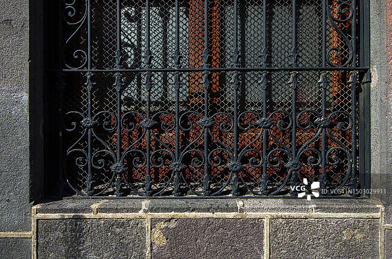 老殖民建筑窗户外，带有卷曲花纹和花卉设计的华丽金属安全格栅图片素材