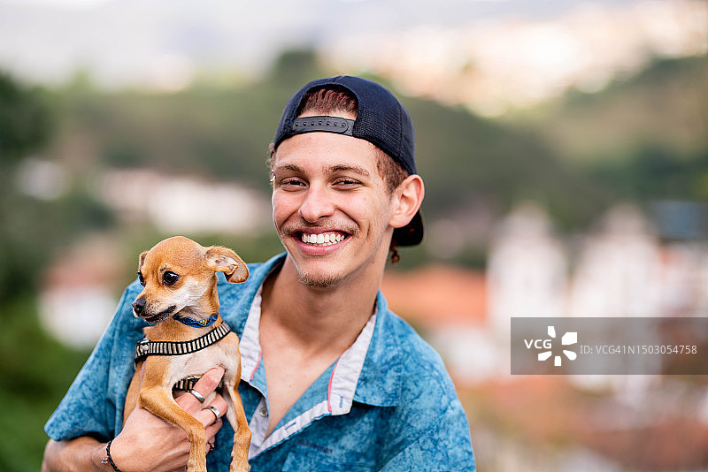 户外抱着可爱吉娃娃的微笑青年图片素材