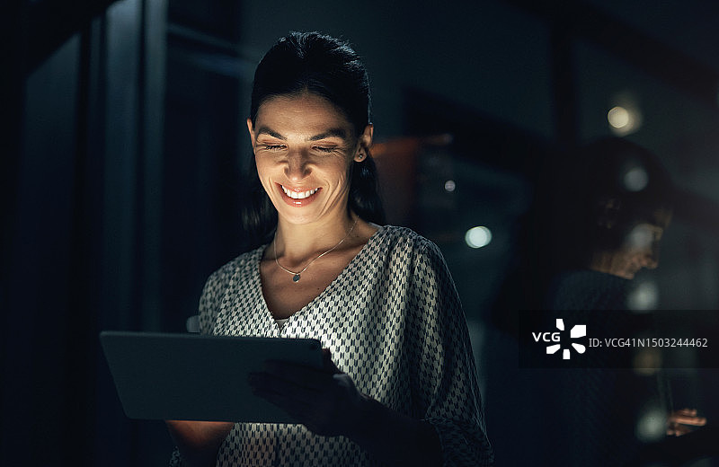 夜晚在代理机构使用平板电脑阅读的职业女性，为营销人员提供应用程序。女商人在线研究技术，在黑暗中使用技术进行在线工作和规划图片素材