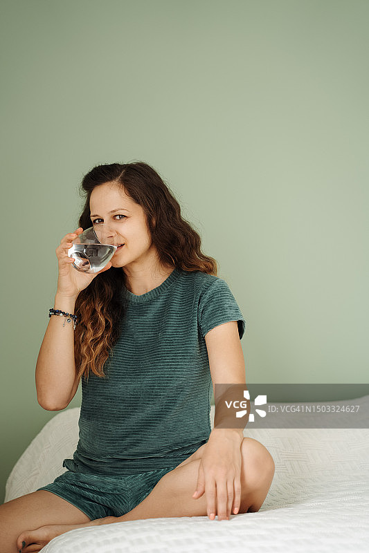 坐在床上微笑喝水的女人图片素材