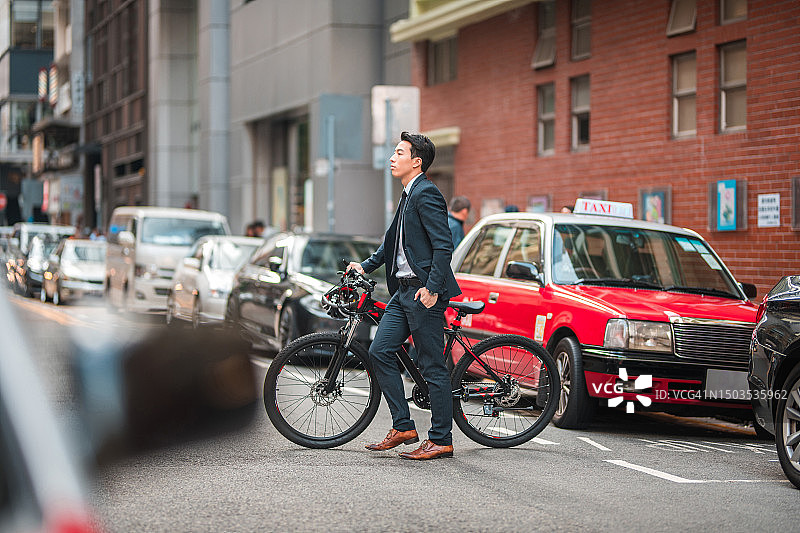 推着自行车过马路的中国年轻男职员图片素材