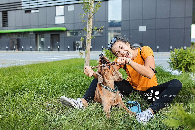 年轻女人在城市公园里和她的狗玩耍图片素材