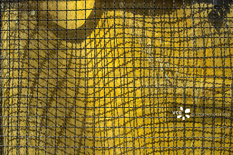 波纹金属丝网在风化的黄色塑料防水布上投下阴影图片素材