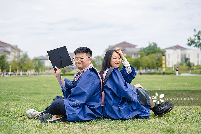 一对年轻夫妇坐在草地上的毕业照图片素材