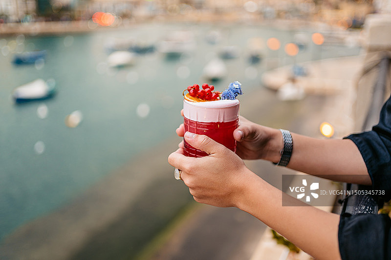 年轻女人在马耳他圣朱利安湾的酒吧露台上喝水果鸡尾酒图片素材