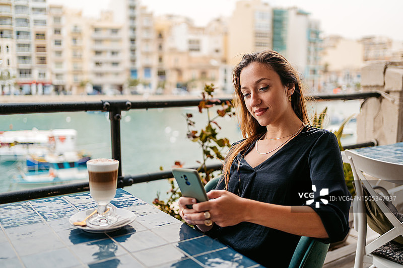年轻女人在马耳他圣朱利安斯湾的咖啡馆露台上使用手机图片素材