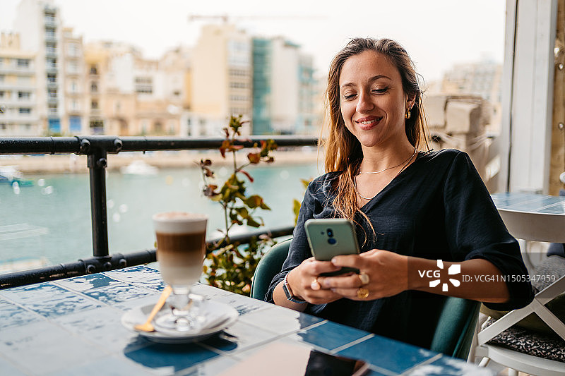 年轻女人在马耳他圣朱利安斯湾的咖啡馆露台上使用手机图片素材