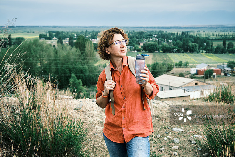女游客站在山上的村庄上方喝水图片素材