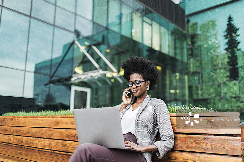 年轻的黑人女商人户外使用笔记本电脑，背景是摩天大楼图片素材