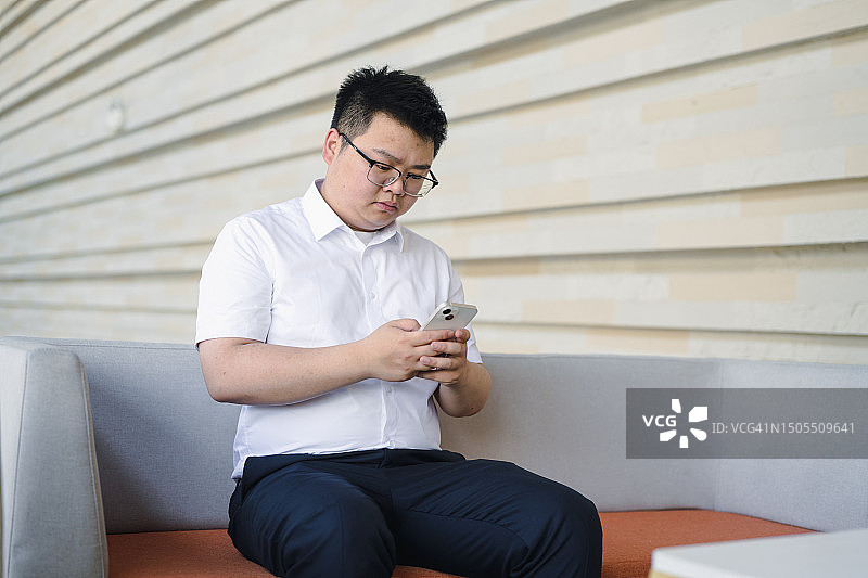 坐在沙发上看手机的年轻男士图片素材