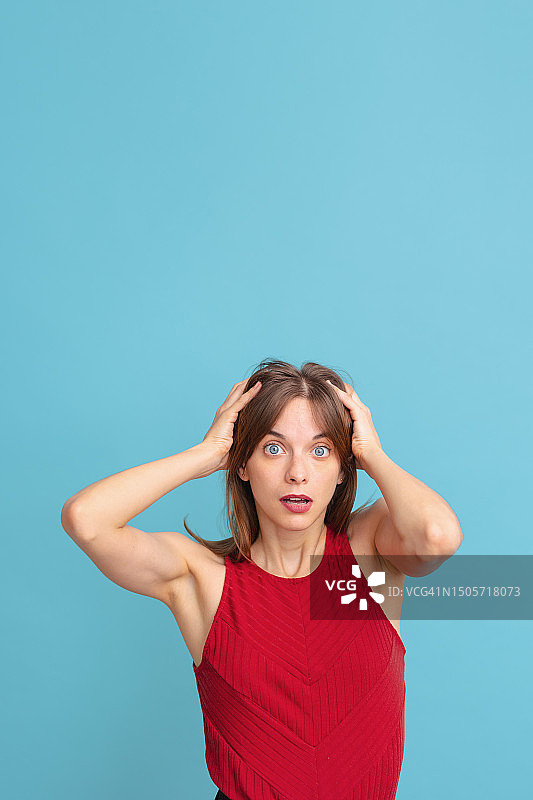 年轻女子双手抱头，蓝色背景，面露绝望图片素材