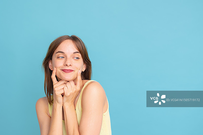 穿着背心的年轻女人微笑地看向一边，手指触摸嘴唇图片素材