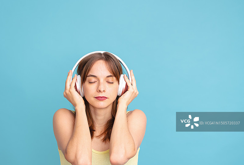 年轻女人在蓝色背景上闭着眼睛听音乐图片素材
