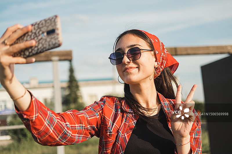 戴着太阳镜和红色头巾的年轻漂亮时髦女孩在阳光明媚的夏日户外自拍图片素材