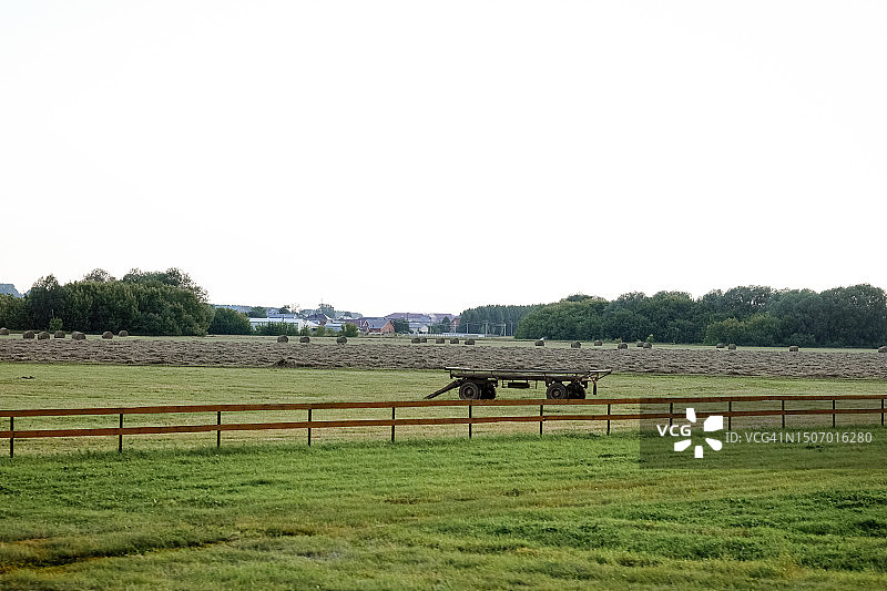 夕阳下，田野里有干草堆和拖拉机拖车，后面是栅栏。美丽的乡村风光图片素材