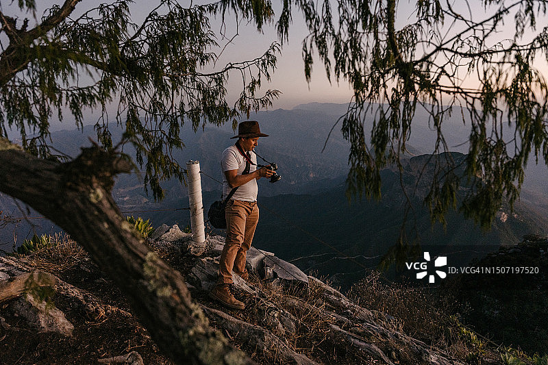 年轻男人欣赏山景并查看相机图片素材