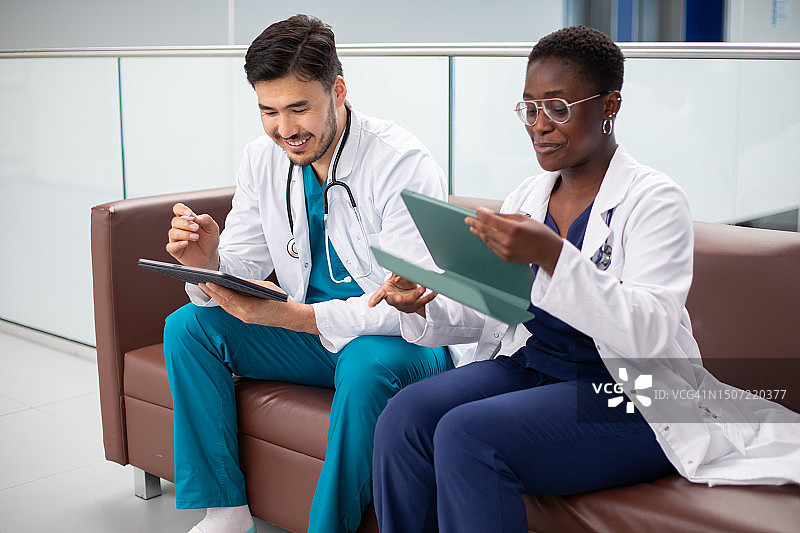 穿着医用磨砂服和实验服的快乐医护人员在沙发上使用平板电脑休息图片素材