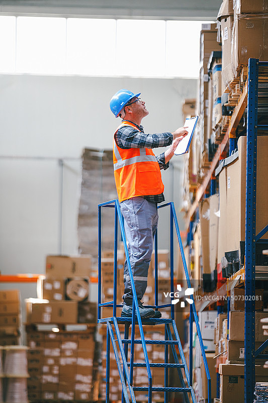 安全高效的仓库运营：工人使用高安全阶梯在货架上存放成品图片素材